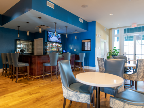 Bar area with blue accents, stools, and tables, adjacent to a light-filled dining space.