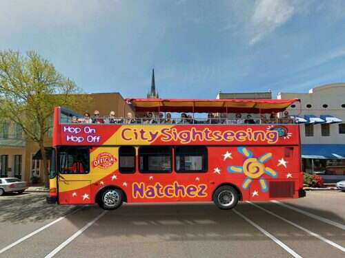 A red and yellow City Sightseeing double-decker bus in Natchez. Passengers on top deck.