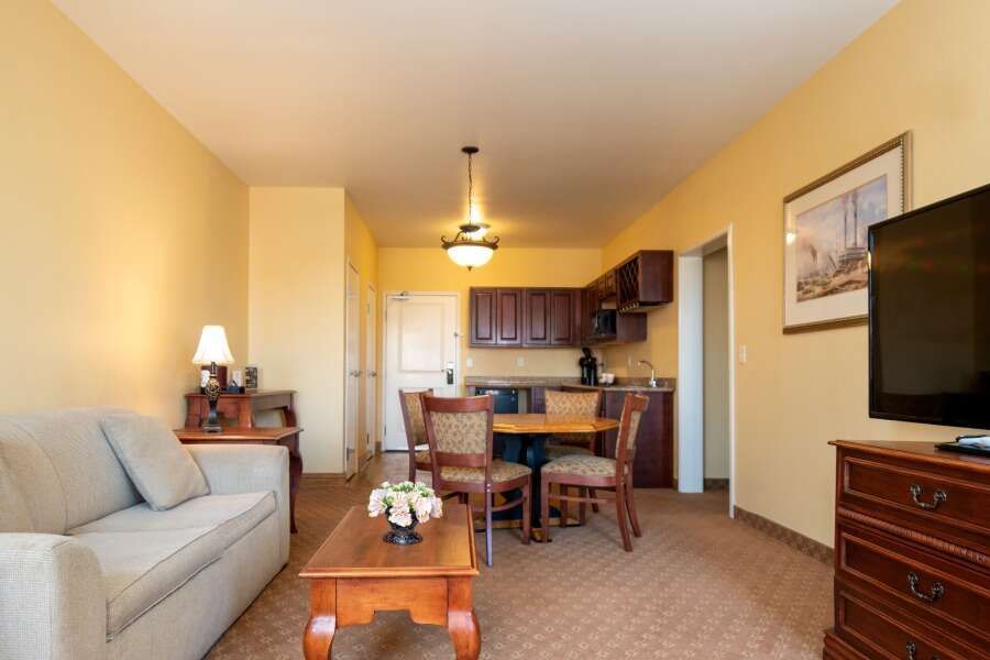 Cozy hotel suite with beige sofa, small kitchen, dining table, and TV.