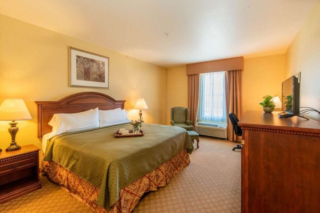 Hotel room with a bed, nightstand, desk, TV, and window with curtains.