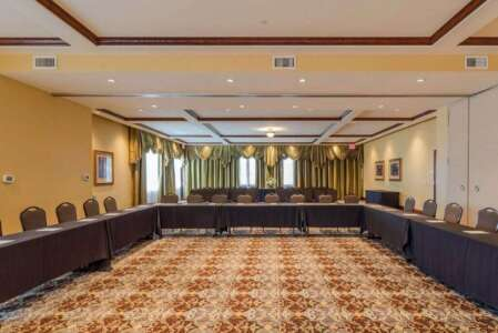 Conference room with U-shaped table setup, beige walls, patterned carpet, and dark draped windows.