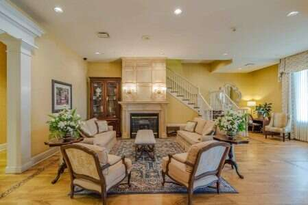 Cozy living room with fireplace, sofas, chairs, and a staircase. Neutral tones with floral accents, in a bright, elegant setting.