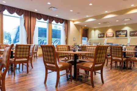 Restaurant dining area with tables, chairs, large windows, and a buffet station. Warm tones and wood flooring.
