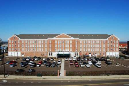 Brick building with a large parking lot. Cars are parked out front under a bright blue sky.