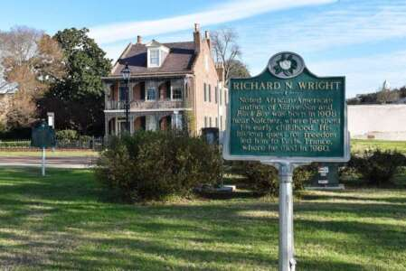 A green historical marker for Richard Wright in front of a two-story brick house with a green lawn.